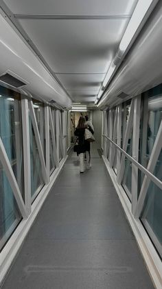 two people walking down a long hallway with windows