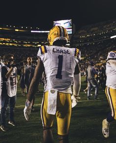 a football player is walking off the field with his team in the background at night