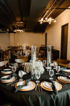 a black table cloth topped with white plates and silverware next to tall vases filled with flowers