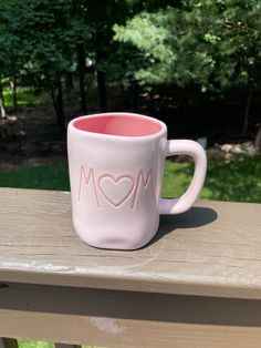 a pink coffee mug with the word mom written on it sitting on a wooden table