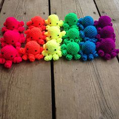 small crocheted stuffed animals are lined up on a wooden surface, all in different colors