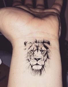 a lion tattoo on the wrist is shown in black and grey ink, with an animal's face drawn across it