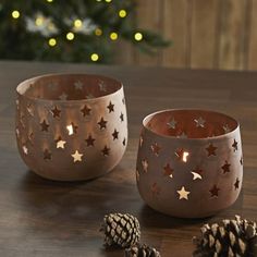 two metal bowls sitting on top of a wooden table next to pine cones and candles