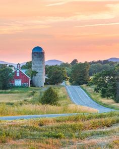 a red barn sits on the side of a country road in front of a sunset