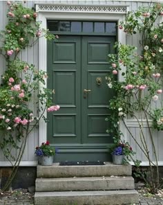 a green door surrounded by pink flowers and greenery