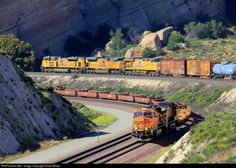 a train traveling down tracks next to a mountain side covered in grass and trees,