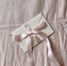 a white envelope with a pink ribbon tied around it on top of a bed sheet