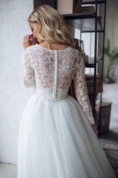 a woman in a white wedding dress is leaning against a wall and looking down at the floor