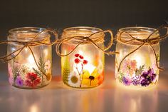 three mason jars with painted flowers and twine tied around the lids are sitting on a table