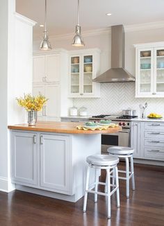 a kitchen with white cabinets and wooden flooring next to two stools in front of an island