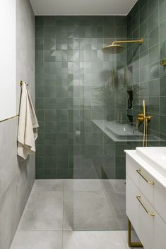 a bathroom with green tiles and gold fixtures on the wall, along with a white sink