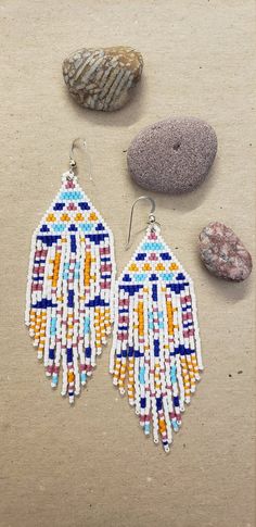 two pairs of beaded earrings sitting on top of a table next to some rocks