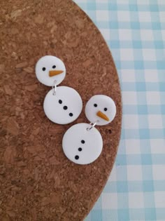 three snowman buttons sitting on top of a cork board next to a blue and white checkered table cloth