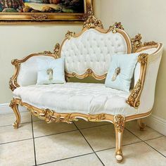 a white and gold couch sitting in front of a painting