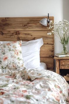 a bed with floral sheets and pillows in a bedroom next to a wooden headboard