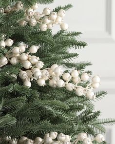 a close up of a christmas tree with white balls on it's branches and pine cones