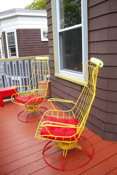 two red and yellow chairs sitting on top of a wooden deck next to a window