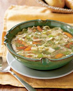 a green bowl filled with soup sitting on top of a white plate next to silverware