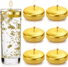 six gold candles are in front of a glass filled with water and some beads on them