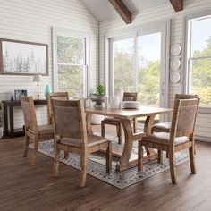 a dining room table with chairs and a rug on the floor in front of windows