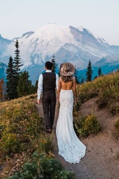 a bride and groom walking down a path towards the mountain top in their wedding attire