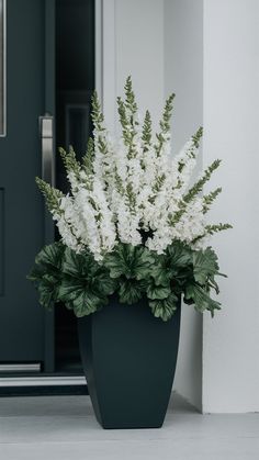 white flowers are in a black vase on the porch