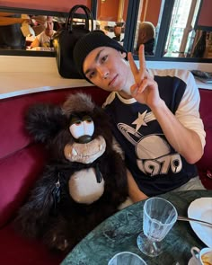 a man sitting at a table with a stuffed animal in front of him and the peace sign