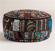 a multicolored patchwork round ottoman with buttons and beads on the top, sitting on a white surface