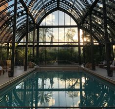 an indoor swimming pool with glass walls and sun shining through the windows on it's sides