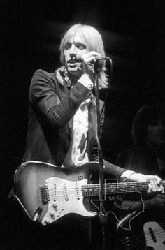 a man holding a guitar while standing next to a microphone and another person on stage