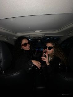 two women sitting in the back of a car talking on their cell phones while wearing sunglasses