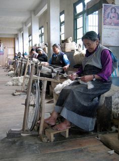 an old woman sitting on top of a wooden bench next to a spinning wheel in a building