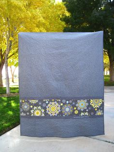 a gray and yellow blanket sitting on top of a cement slab in front of trees