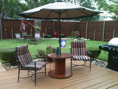 two chairs and an umbrella are sitting on a wooden deck in the backyard with a bbq