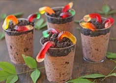 three glasses filled with dirt and gummy bears on top of a table next to leaves