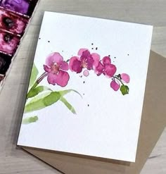 a card with pink flowers on it next to some paintbrushes and watercolors