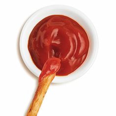 a small white bowl filled with ketchup on top of a wooden stick