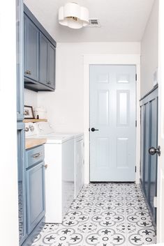 a white and blue kitchen with tile flooring, cabinets, and door leading to the washer and dryer