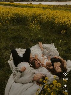 three women laying on a blanket in the middle of a field full of yellow flowers