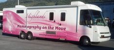 a pink and white truck parked in a parking lot next to a mountain with trees