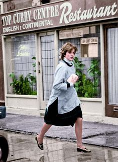 a woman running down the street in front of a restaurant on a rainy day with an umbrella over her head