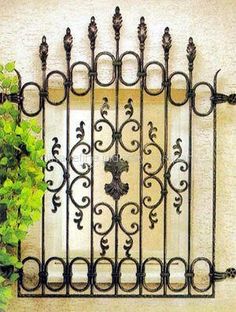 an iron fence with vines and flowers on the side of a building in front of a window