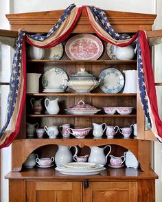 an old china cabinet with plates and cups on it's shelves, decorated in red, white and blue