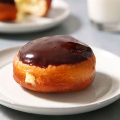 a chocolate covered doughnut sitting on top of a white plate next to a glass of milk