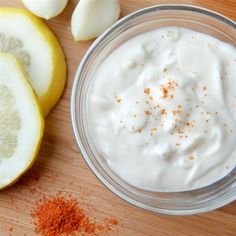 a bowl of yogurt next to sliced lemons on a wooden cutting board