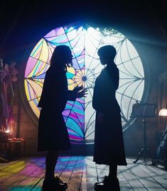 two people standing in front of a stained glass window with lights coming from behind them