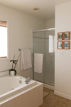 a bathroom with a bathtub, shower and pictures on the wall above it's glass door