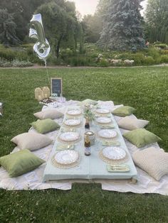 a table set up with plates and silverware on it in the middle of a field