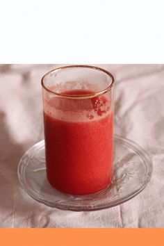 a glass filled with red liquid sitting on top of a table next to a plate