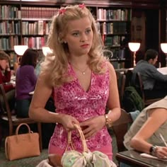 a woman in a pink dress holding a basket and sitting at a table with other people